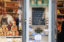 an italian store front selling food; an employee inside is sticking out his tongue playfully