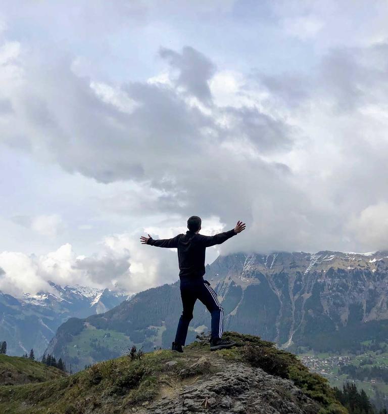 A student with outstretched arms atop a mountain