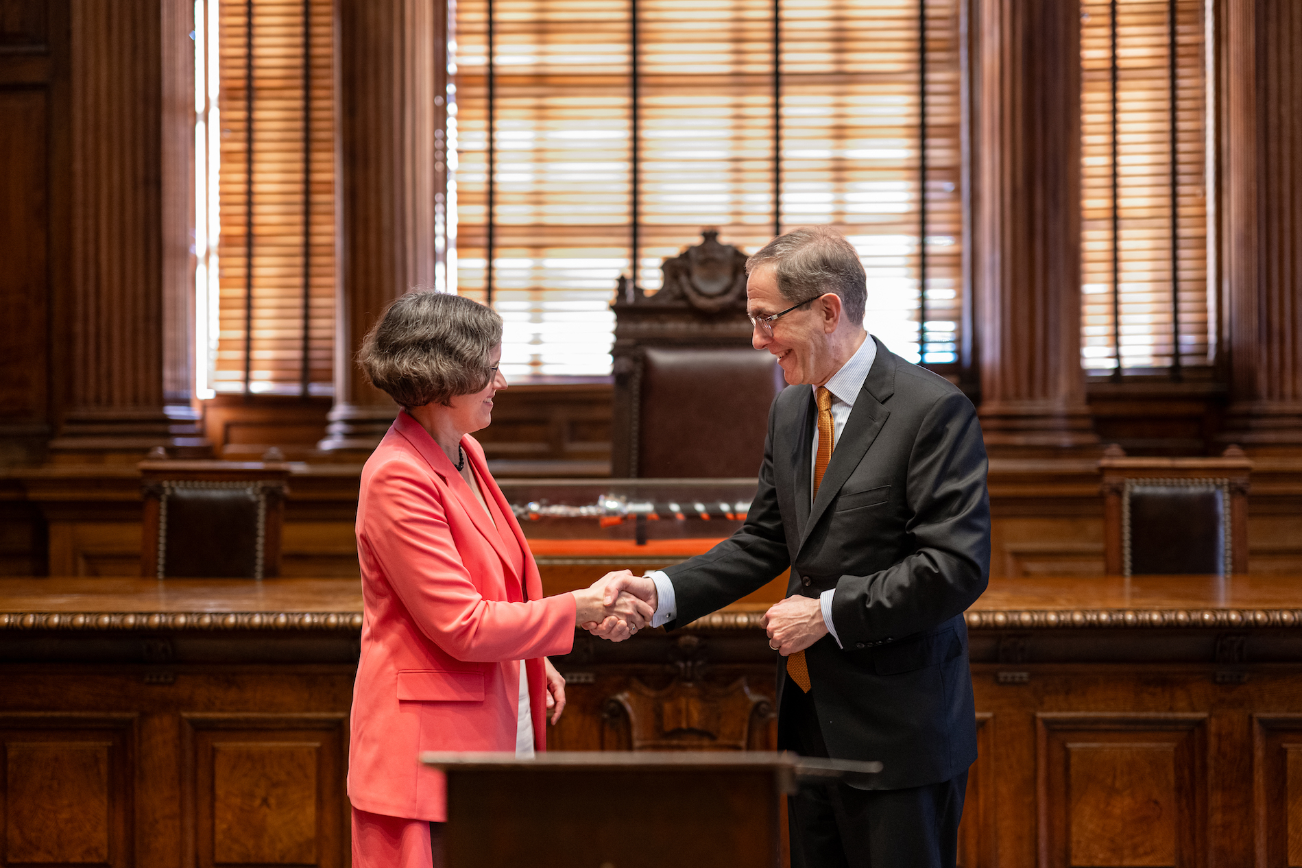 A woman and a man shake hands behind a lectern. 