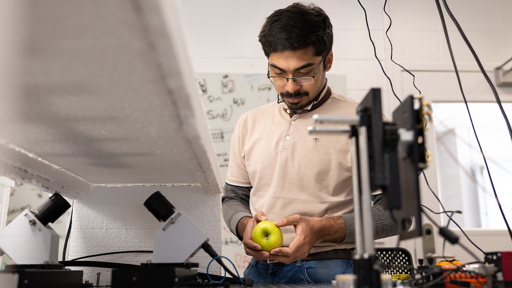 A man stands in the lab looking at an apple.
