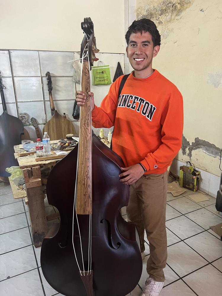 A young man in a bright Princeton sweatshirt holds an upright bass