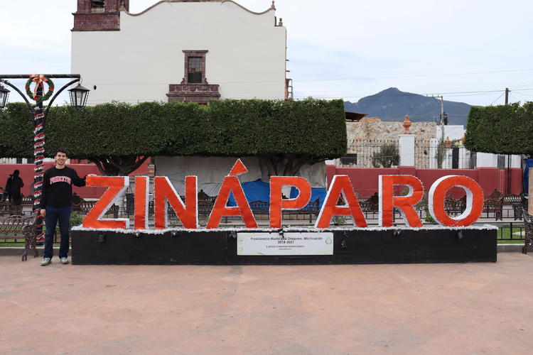 Carlos stands next to a large sign reading Zinaparo
