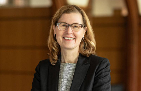 An image of Professor Janet Currie smiling behind a brown wooden background