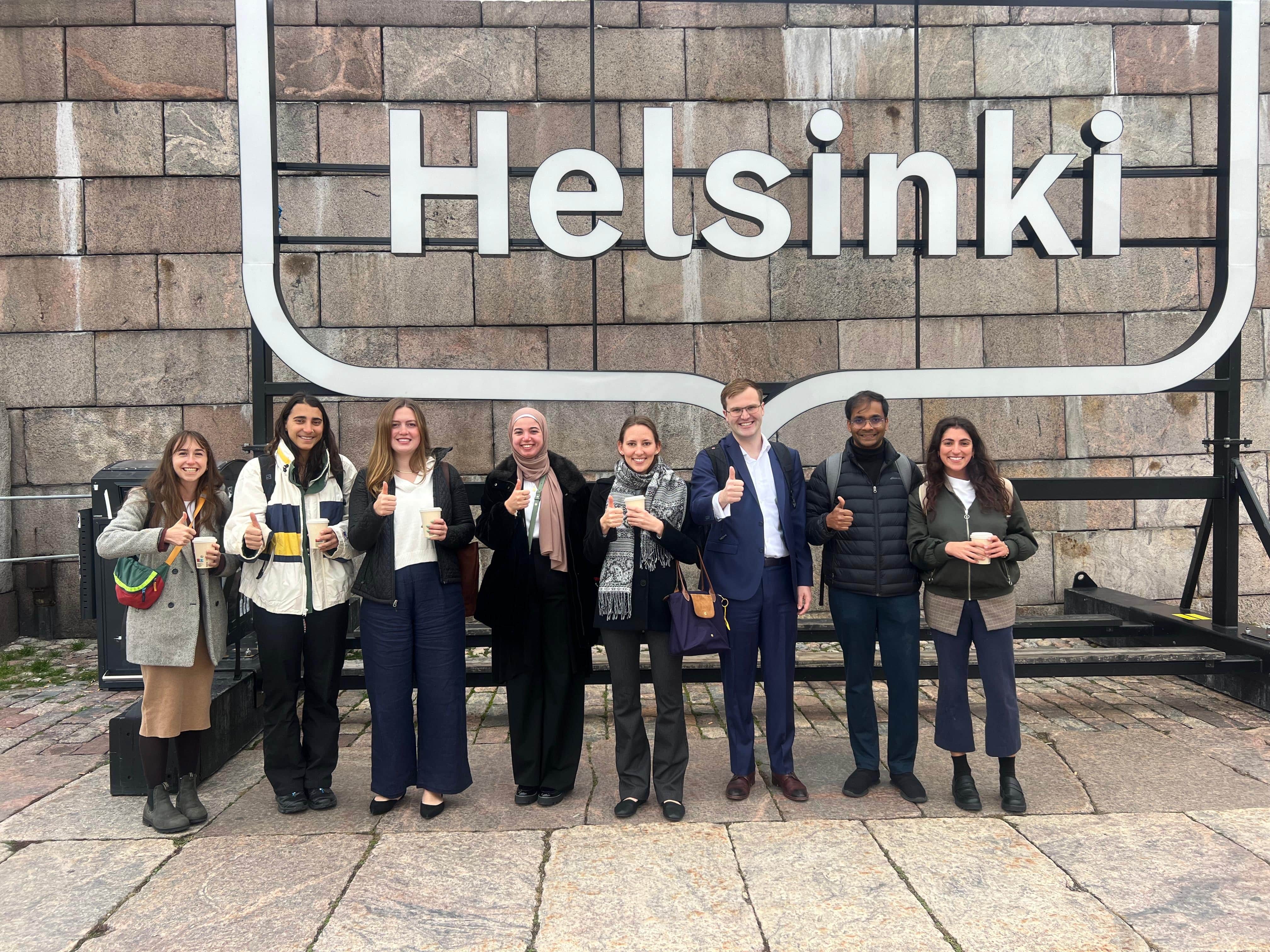 An image of SPIA students smiling behind a sign that says Helsinki