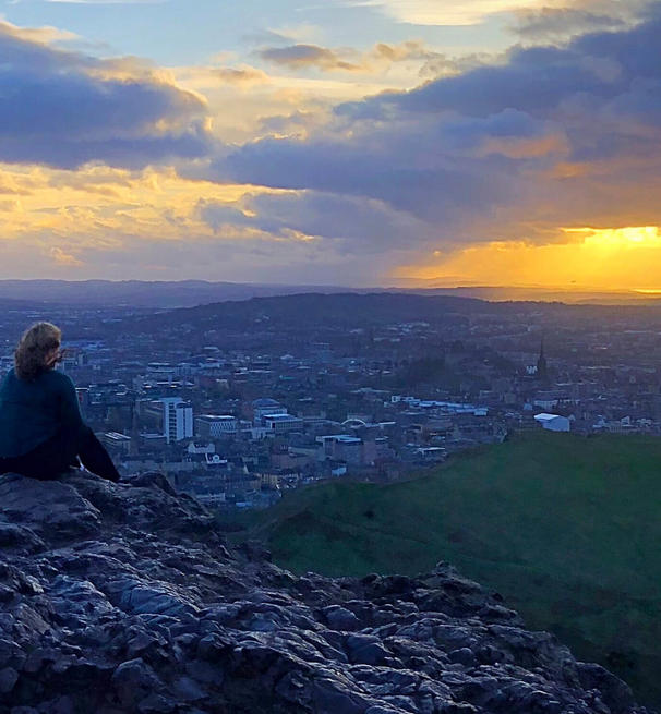 A woman atop a mountain gazes over a Scottish city