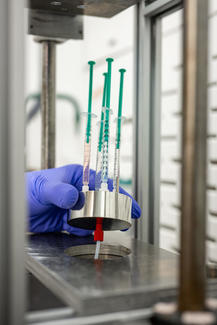 a gloved hand works with pipettes in a lab.