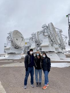 Three masked figures stand next to giant satellite dishes