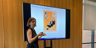 A woman gives a presentation before a flat screen with an illustration on it