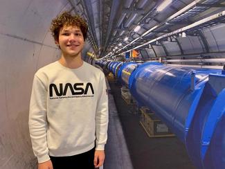A male student in a NASA shirt stands beside a blue pipeline