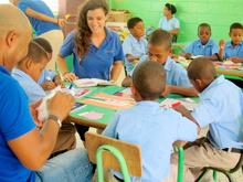 Two Princeton in Latin America workers sit at a table of young children in school.