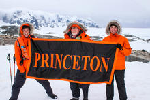 Three men in bright orange hold up a black-and-orange Princeton banner in antartica.