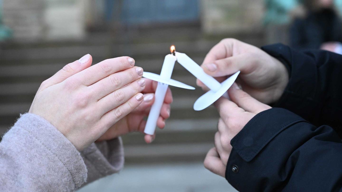 Two hands in close up, both with memorial candles burning