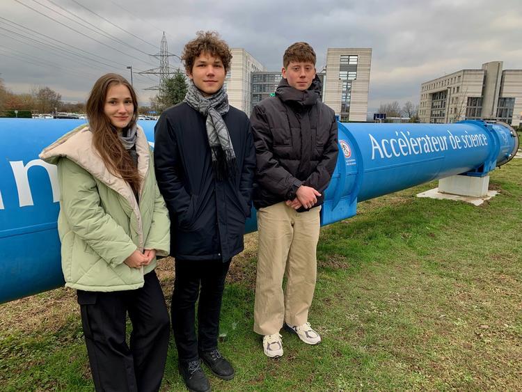 Three students stand beside a blue pipeline