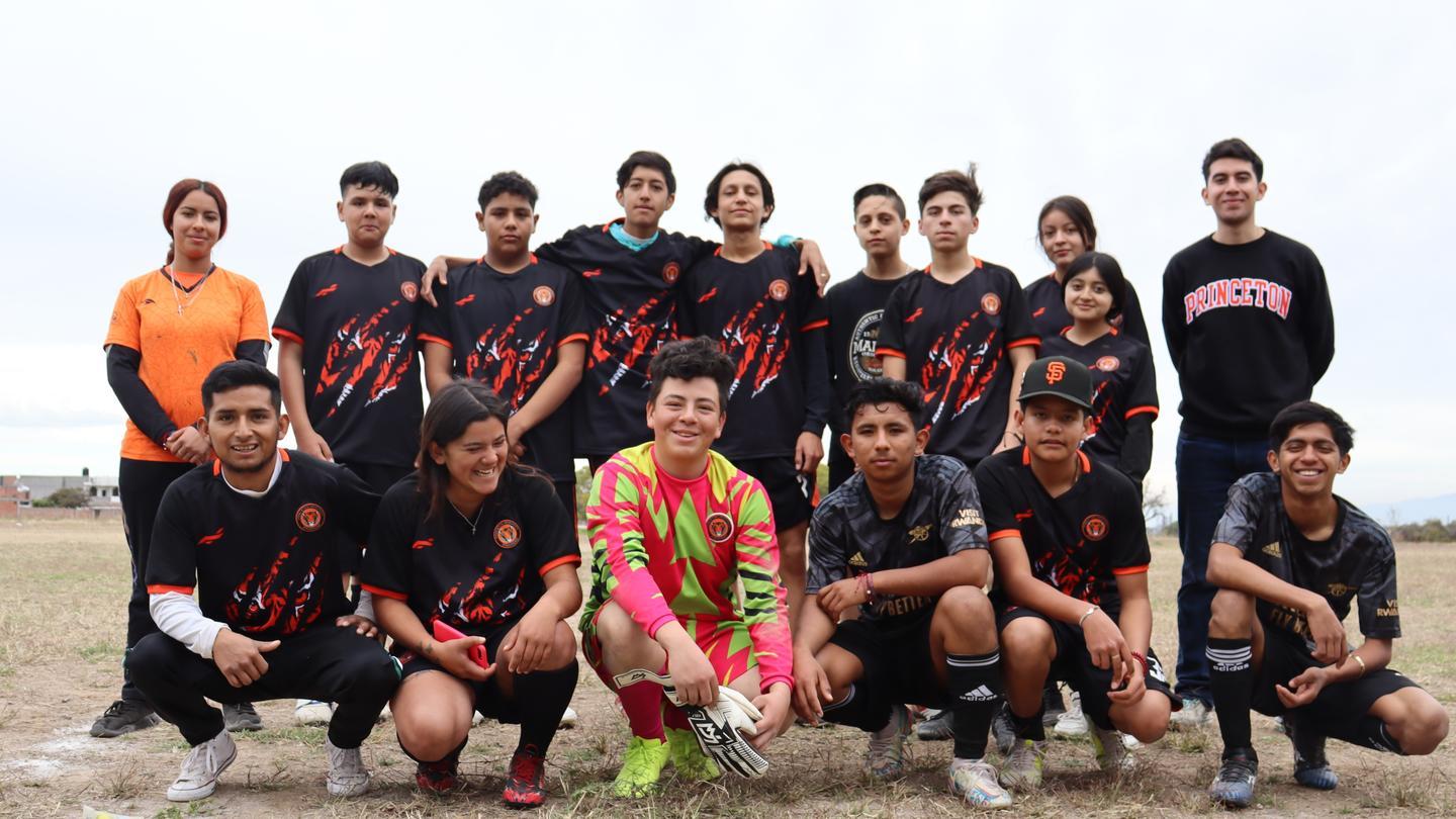 A group of youngsters in soccer jerseys pose. Carlos is to the far right.