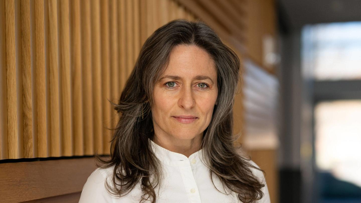 A headshot of Betsy Levy Paluck infront of a wooden background