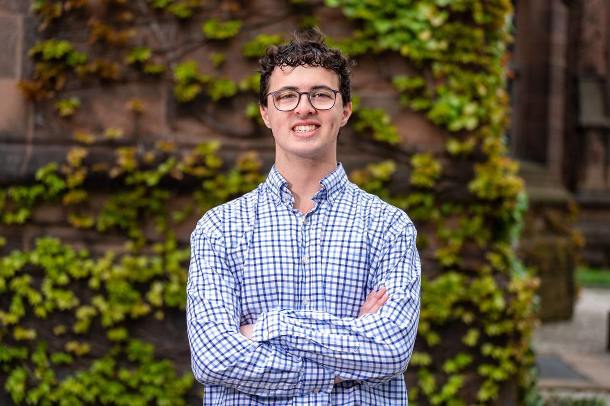 A picture of Senior Shane Patrick wearing a blue and white plaid button up shirt in front of the Easy Pyne building covered with green ivy