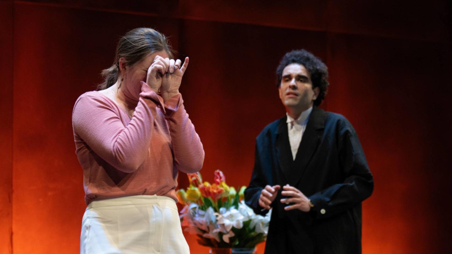 A distressed female actor wearing a long pink shirt while a male actor dressed in a black suit tries to talk to her