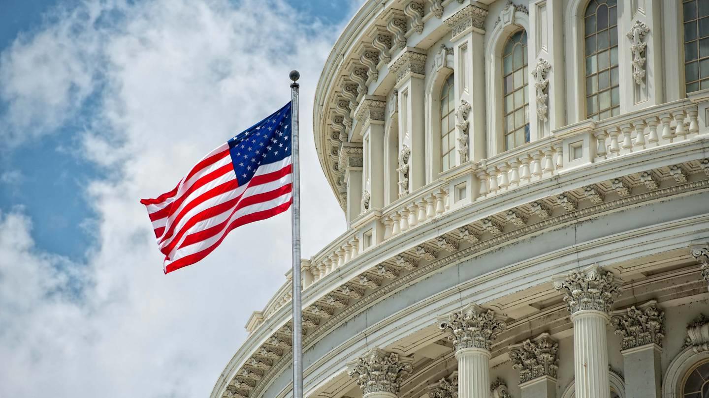 A stock photo of the us capitol with a flag in the foreground