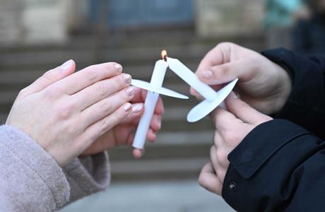 Two hands in close up, both with memorial candles burning