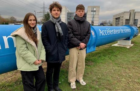 Three students stand beside a blue pipeline