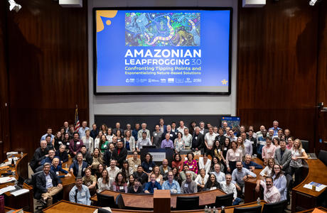 A group is assembled in a Princeton bowl auditorium under a projector showing the Amazonian Leapfrogging 3.0 promotional poster