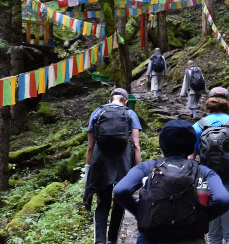 several students trek up a moss-covered mountain in China, which is strewn with colorful flags 